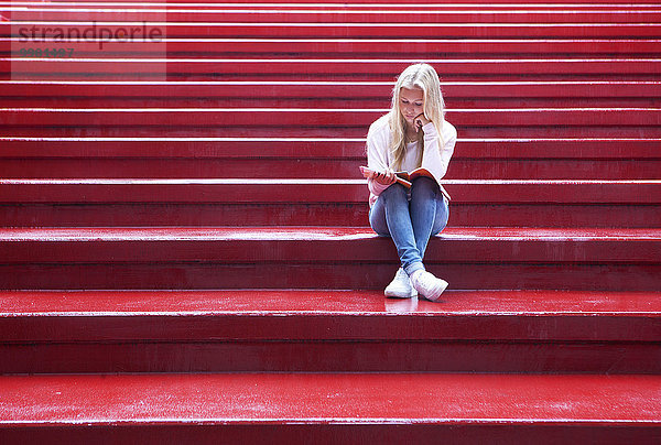 Teenagerin sitzt auf einer roten Treppe und liest