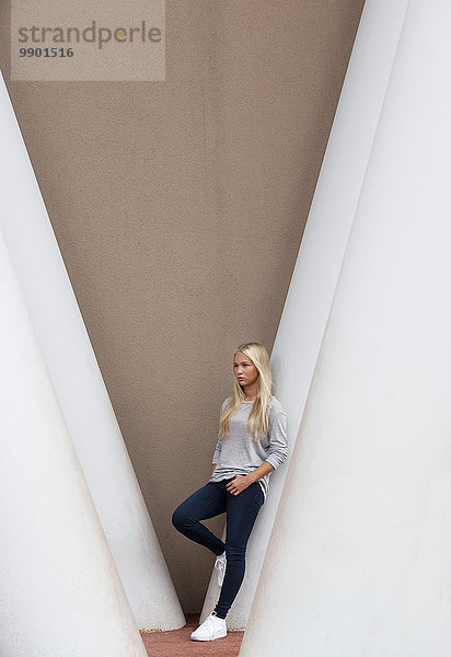 Porträt einer blonden Teenagerin  die sich auf eine Betonsäule stützt.