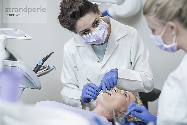 Zahnärztin untersucht Patientin mit Mundspiegel