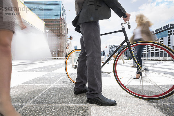 Geschäftsmann  der mit dem Fahrrad zwischen einer Menschenmenge in einer Stadt spazieren geht.