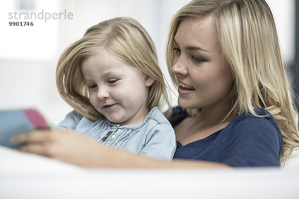 Mutter und Tochter sitzen auf einer Couch und lesen ein Buch.