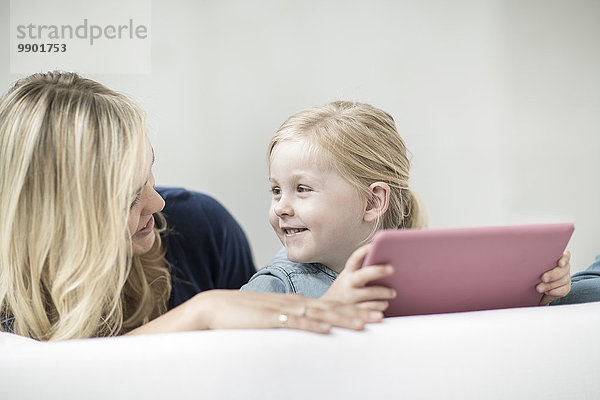 Mutter und kleine Tochter auf Couch mit digitalem Tablett