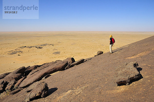 Mann blickt vom Monolithen Aicha auf die flache Wüste  Region Adrar  Mauretanien  Afrika