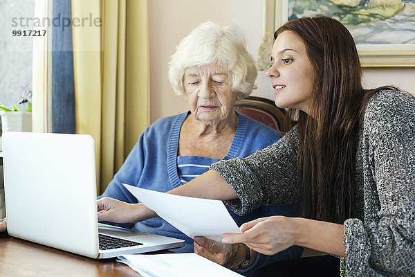 Großmutter und Enkelin mit Dokument mit Laptop zu Hause