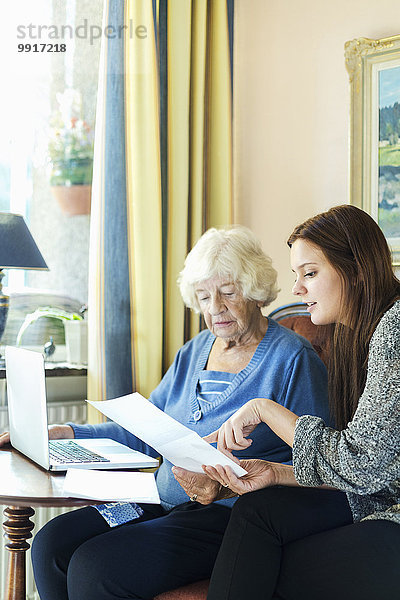 Großmutter und Enkelin lesen das Dokument  während sie zu Hause den Laptop benutzen.