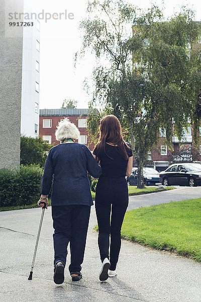 Vollständige Rückansicht einer älteren Frau  die mit ihrer Enkelin auf dem Fußweg geht.