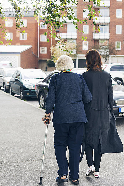 Rückansicht einer älteren Frau  die mit ihrer Enkelin auf dem Bürgersteig in der Stadt spazieren geht.