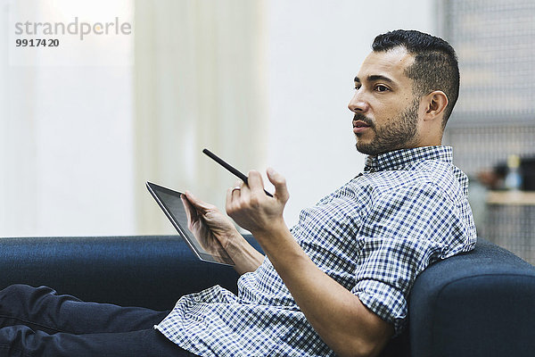 Seitenansicht des Geschäftsmannes mit digitalem Tablett beim Entspannen auf dem Sofa im Büro