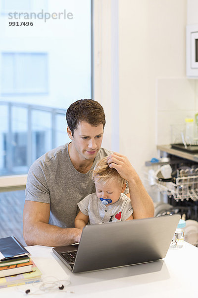 Baby Junge sitzend mit Vater mit Laptop am Tisch im Haus