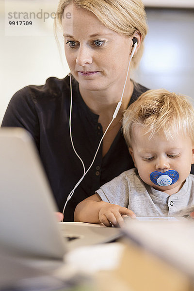 Mutter mit Kleinkind beim Musikhören auf dem Laptop zu Hause