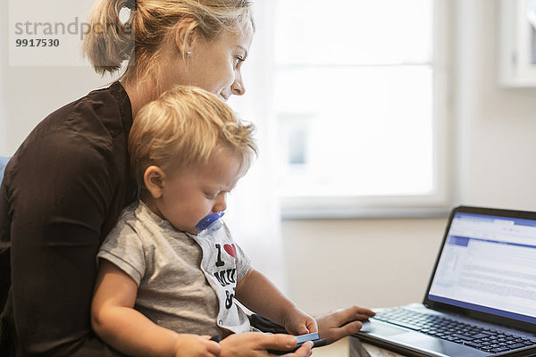 Mutter mit Kleinkind mit Laptop zu Hause