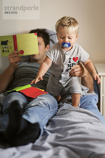 Vater liest Buch  während er das Baby im Bett hält.