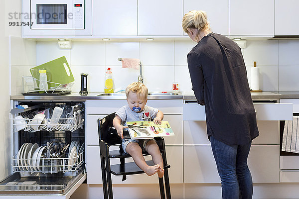 Mutter arbeitet in der Küche  während der Junge auf dem Hochstuhl sitzt.