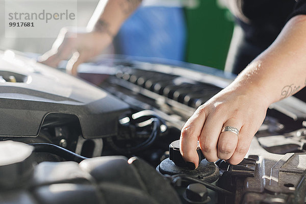 Abgeschnittenes Bild einer weiblichen Mechanikerin  die das Kühlmittel im Auto öffnet