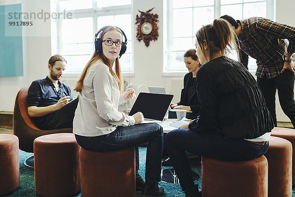 Geschäftsfrau schaut weg  während sie mit Kollegen im Kreativbüro sitzt.