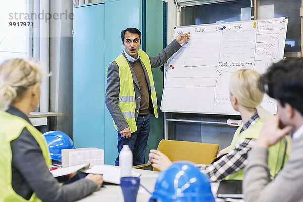 Reife männliche Arbeitskraft erklärt den Kollegen in der Fabrik den Plan auf dem Whiteboard.
