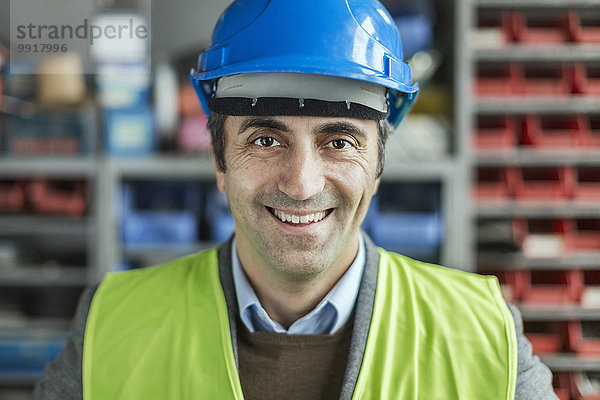 Porträt eines fröhlichen reifen Handarbeiters mit Schutzhelm in der Fabrik