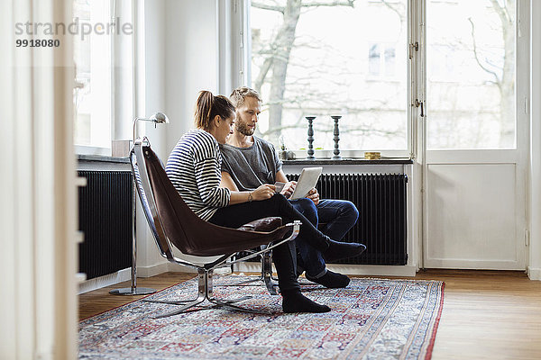 Volle Länge der Paare online einkaufen  während sie zu Hause auf Stühlen sitzen.