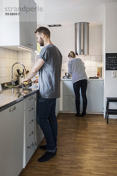 Mann wäscht Soßenpfanne  während Frau im Hintergrund in der Küche steht.