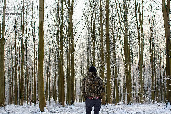 Rückansicht des jungen Mannes im schneebedeckten Wald mit kahlen Bäumen