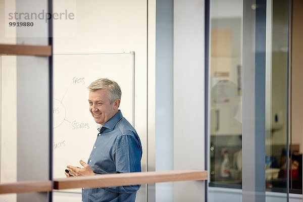 Ausgereifter Geschäftsmann präsentiert auf Büro-Whiteboard