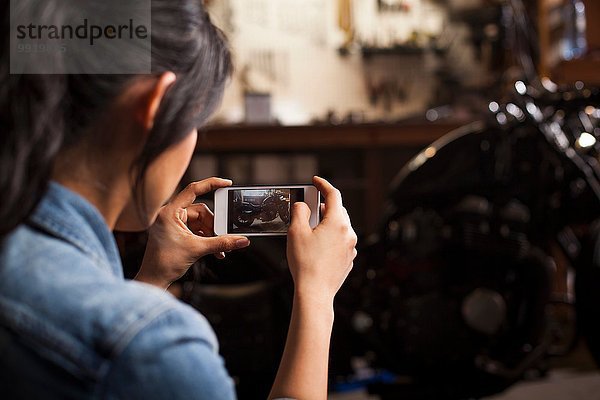 Mechanikerin in der Werkstatt  Fotografieren des Motorrads mit dem Smartphone