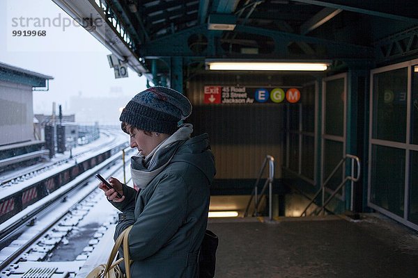 Mittlere erwachsene Frau am Bahnhof stehend mit dem Handy