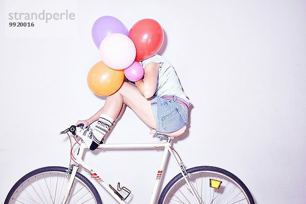 Studioaufnahme einer jungen Frau  die auf einem Fahrrad sitzt und sich hinter Luftballons versteckt.