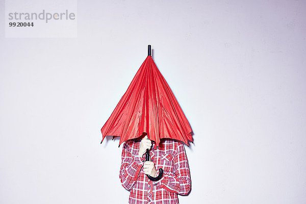 Studioaufnahme einer jungen Frau  die einen roten Regenschirm über den Kopf hält.
