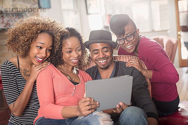 Vier erwachsene Freunde sitzen auf dem Sofa und schauen sich das digitale Tablett an.