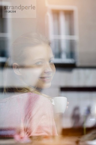 Porträt einer jungen Frau  die Kaffee trinkt und durchs Caféfenster schaut
