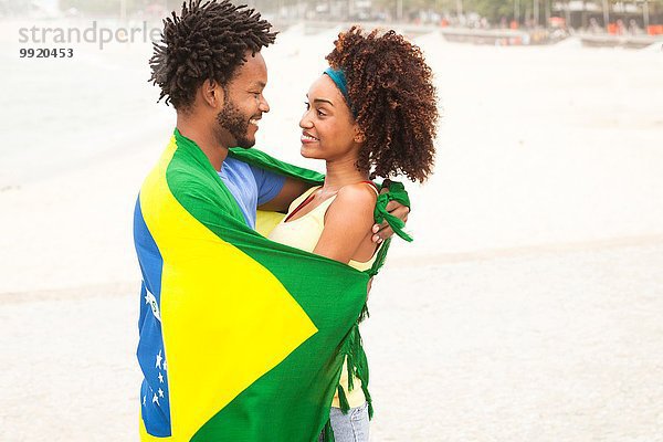 Lächelndes Paar in brasilianischer Flagge am Strand von Ipanema  Rio De Janeiro  Brasilien