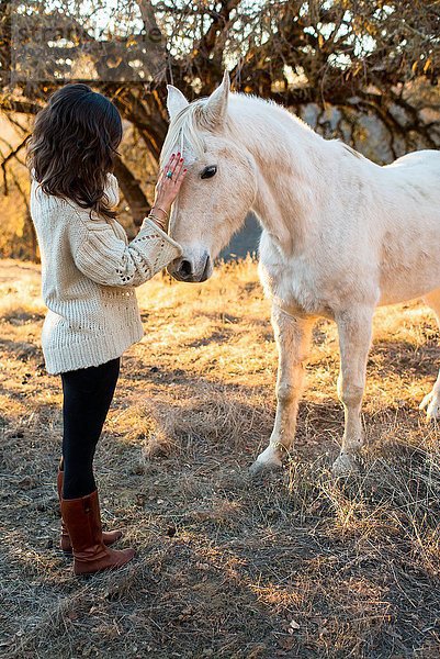 Junge Frau streichelt weißes Pferd im Feld
