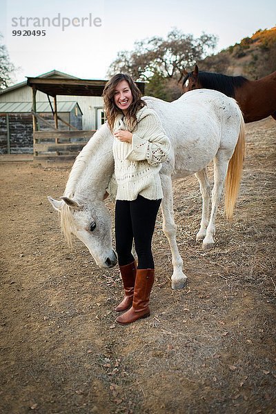 Porträt einer jungen Frau  die ein weißes Pferd streichelt.
