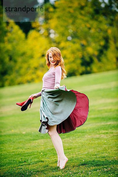 Porträt einer jungen Tänzerin  die den Rock und die roten High Heels im Park hält.