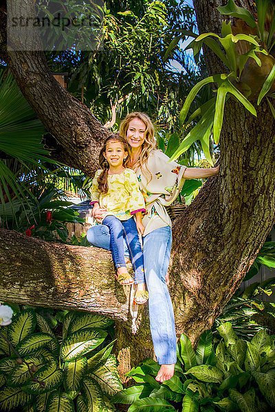 Mutter und Tochter sitzen auf einem Gartenbaumzweig