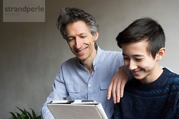 Vater und jugendlicher Sohn lesen digitales Tablett