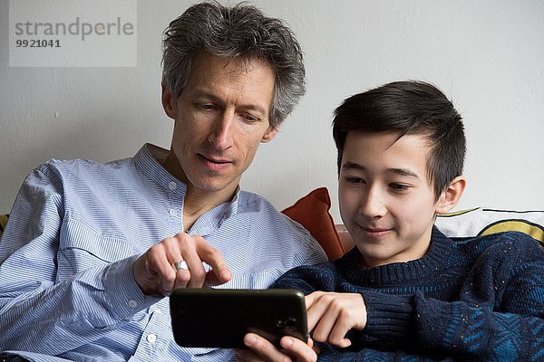 Teenager Junge und Vater spielen Smartphone-Spiel auf dem Sofa