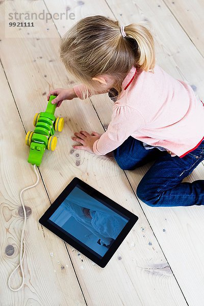 Mädchen mit digitalem Tablett  Spielzeug auf Holzfußboden