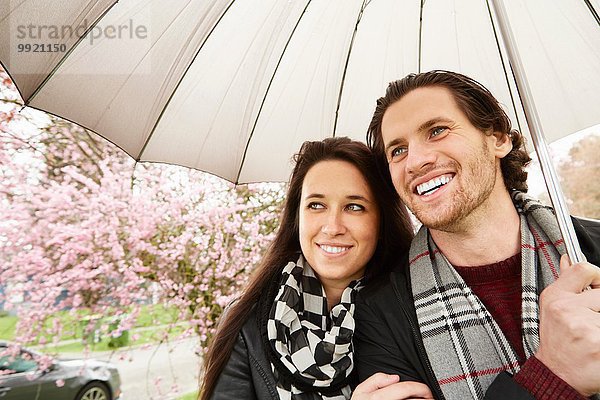 Junges Paar beim Spaziergang im Park mit Regenschirm