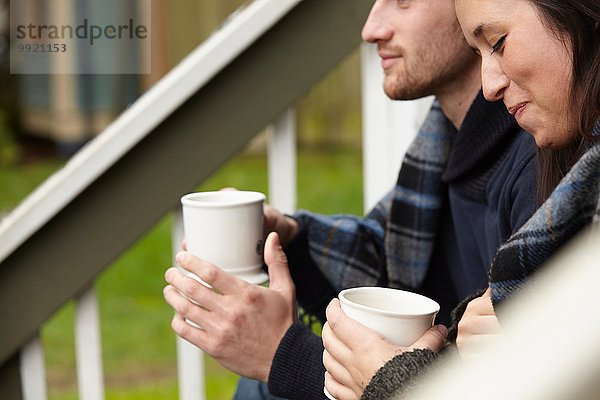 Ausschnitt eines jungen Paares  das auf der Veranda sitzt und Kaffee trinkt.