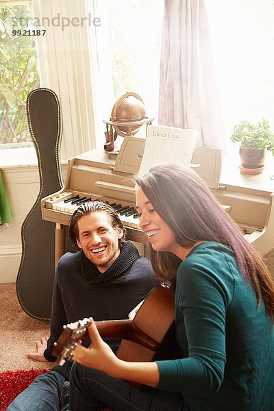 Junges Paar spielt Akustikgitarre im Wohnzimmer