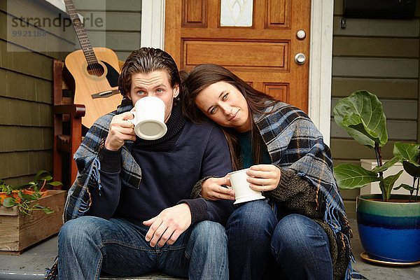 Junges Paar auf der Veranda  eingehüllt in eine Decke  die Kaffee trinkt.