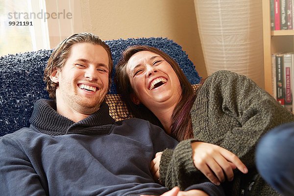 Junges Paar lacht auf dem Wohnzimmersofa