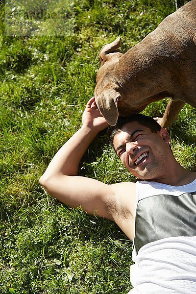 Draufsicht eines jungen Mannes  der mit einem Hund auf Gras spielt.
