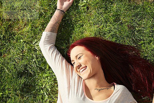 Draufsicht einer jungen Frau  die auf Gras liegt und lacht.
