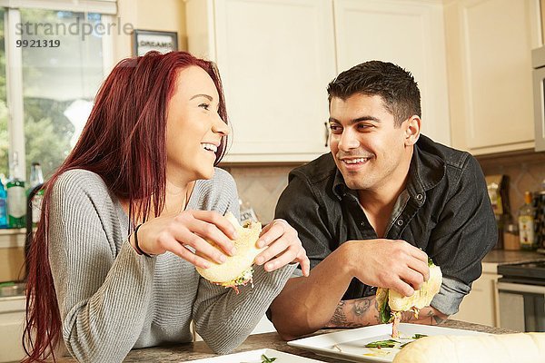 Junges Paar isst Sandwiches an der Küchentheke