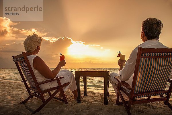 Seniorenpaar mit Getränken am Strand  Malediven