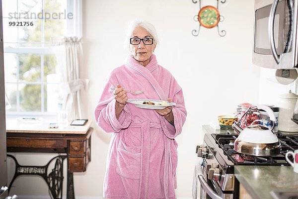 Seniorin steht in der Küche und hält den Teller mit dem Essen.