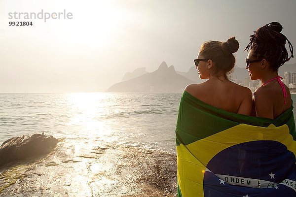 Rückansicht von zwei jungen Frauen in brasilianischer Flagge  Strand von Ipanema  Rio De Janeiro  Brasilien